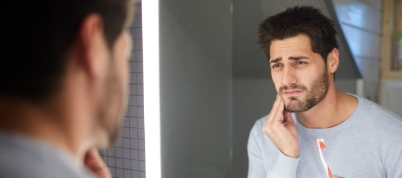 Man holding his toothbrush and touching his cheek in pain